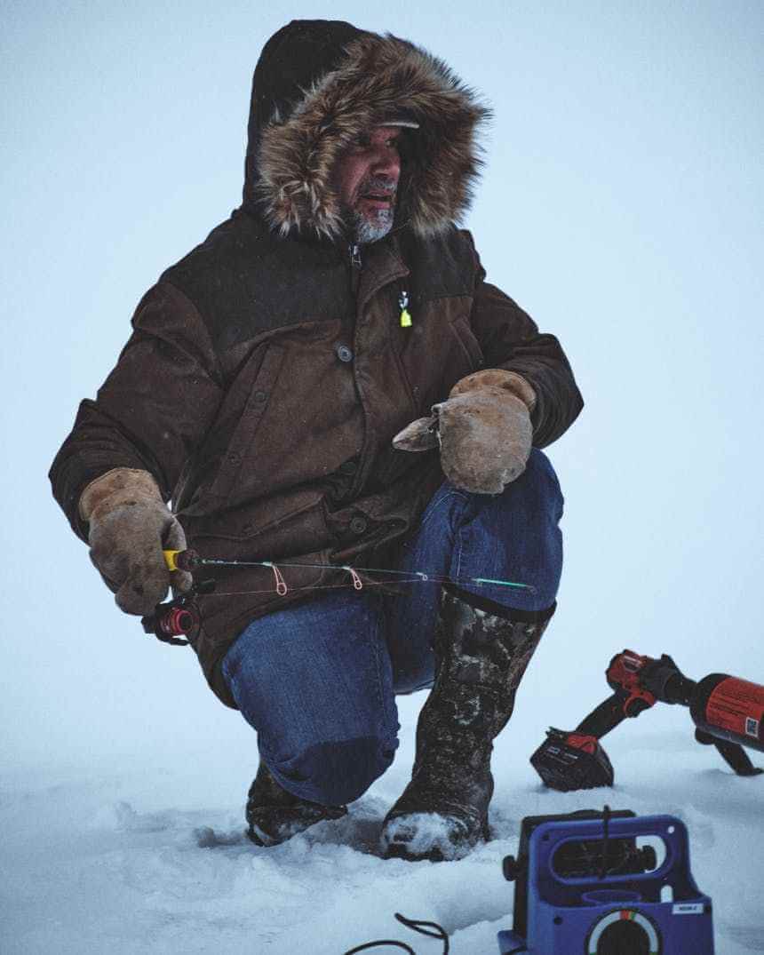 Инструктор IceClub по зимней рыбалке на фоне заснеженного берега.